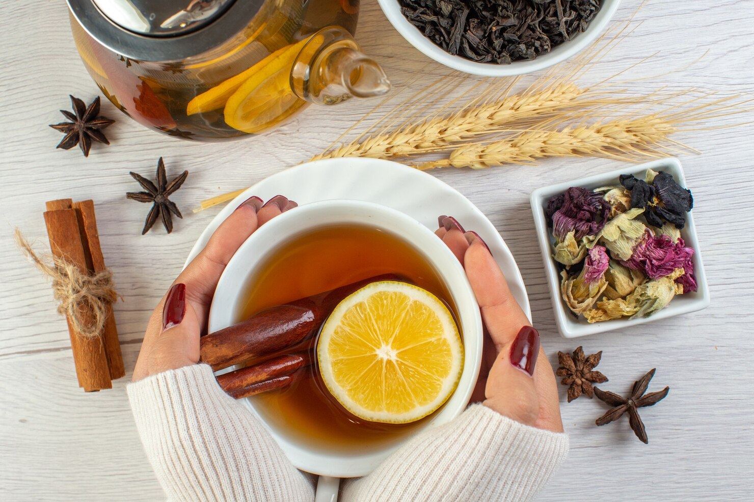 Person holding a warm cup of herbal tea surrounded by fresh botanical ingredients